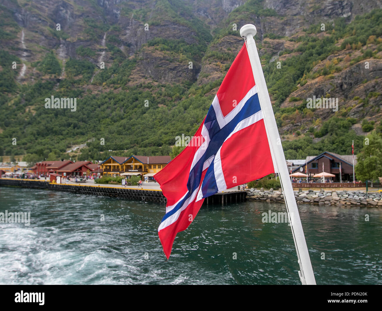 Norwegian flag is flying at the stern of a boat travelling through a fjord. Stock Photo