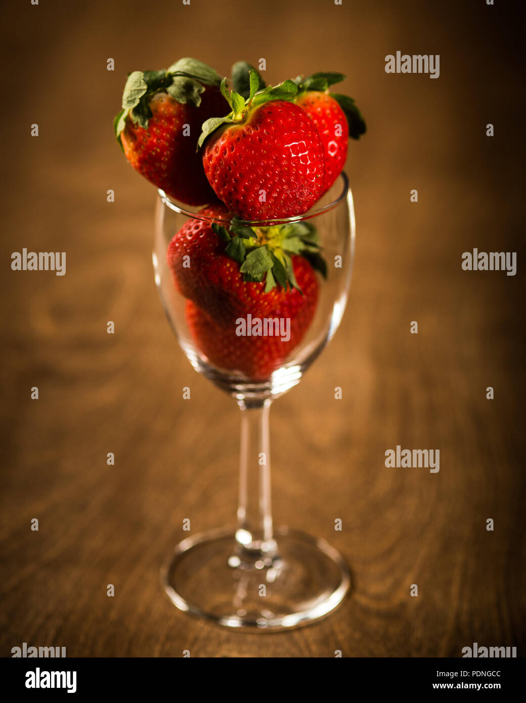 Strawberries in wine glass sitting on dark wood table Stock Photo - Alamy