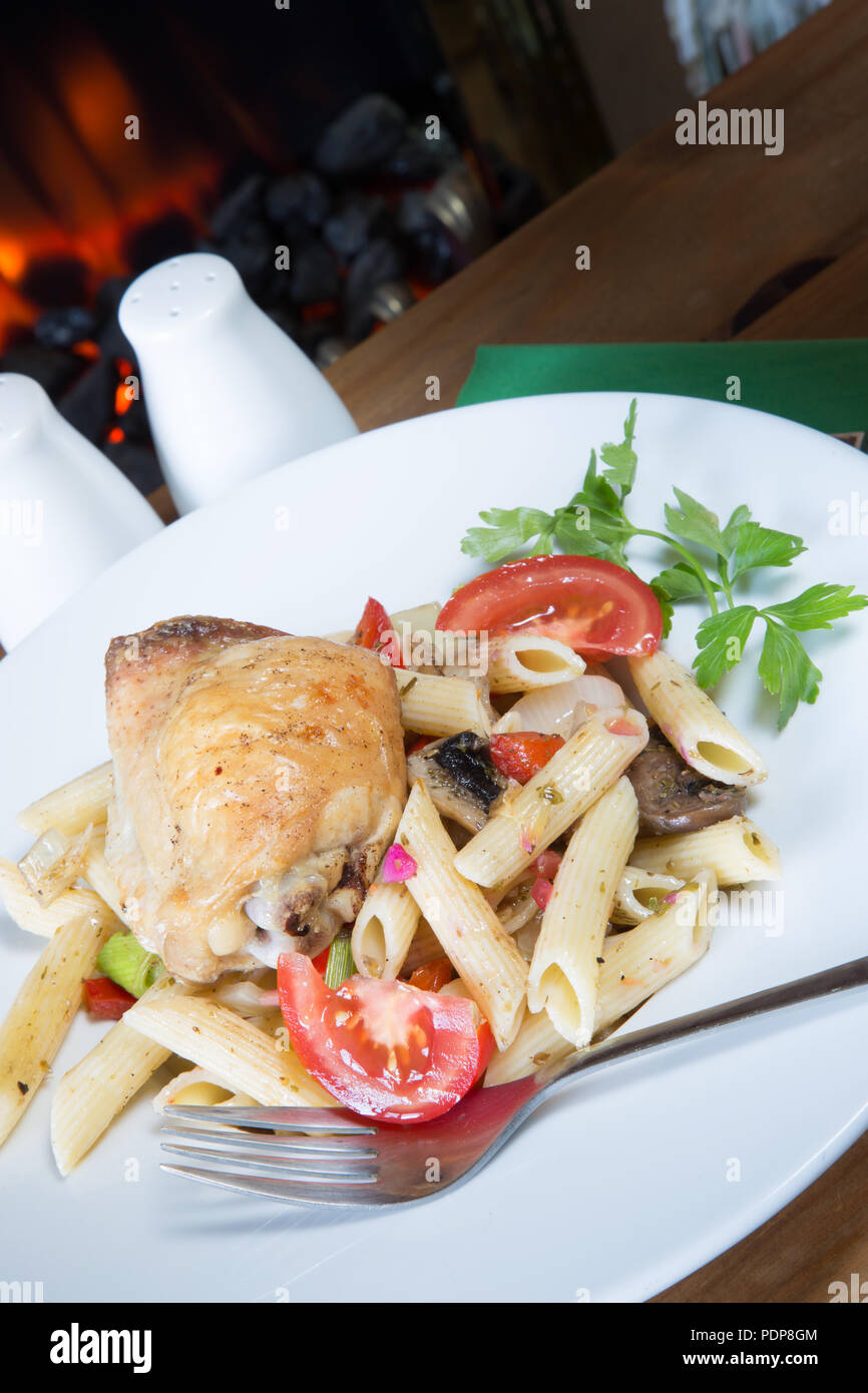 A plated meal of Pollo e Penne, Garlic infused roast Chicken thigh with Penne pasta and tomato, onion and mushroom Stock Photo
