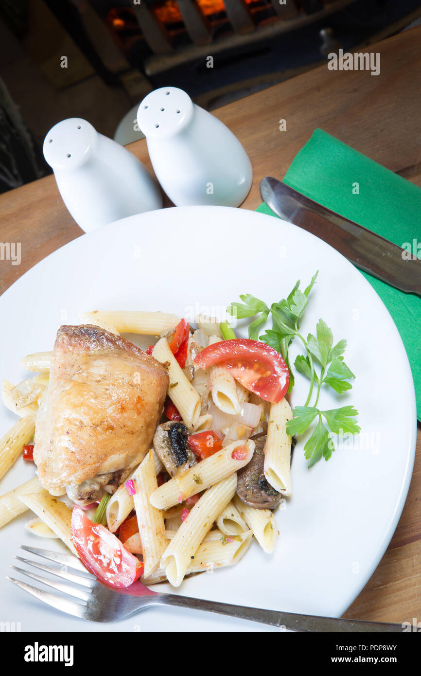 A plated meal of Pollo e Penne, Garlic infused roast Chicken thigh with Penne pasta and tomato, onion and mushroom Stock Photo