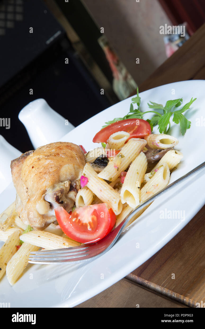 A plated meal of Pollo e Penne, Garlic infused roast Chicken thigh with Penne pasta and tomato, onion and mushroom Stock Photo