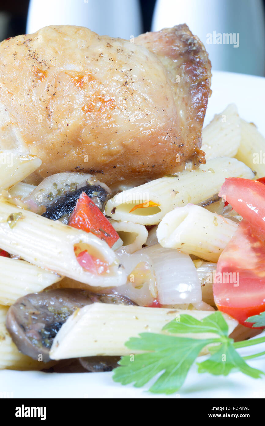 A plated meal of Pollo e Penne, Garlic infused roast Chicken thigh with Penne pasta and tomato, onion and mushroom Stock Photo