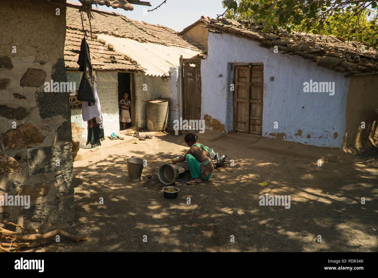 A young womann washing dishes in a typical village somewhere in rural Gujarat in Western India Stock Photo