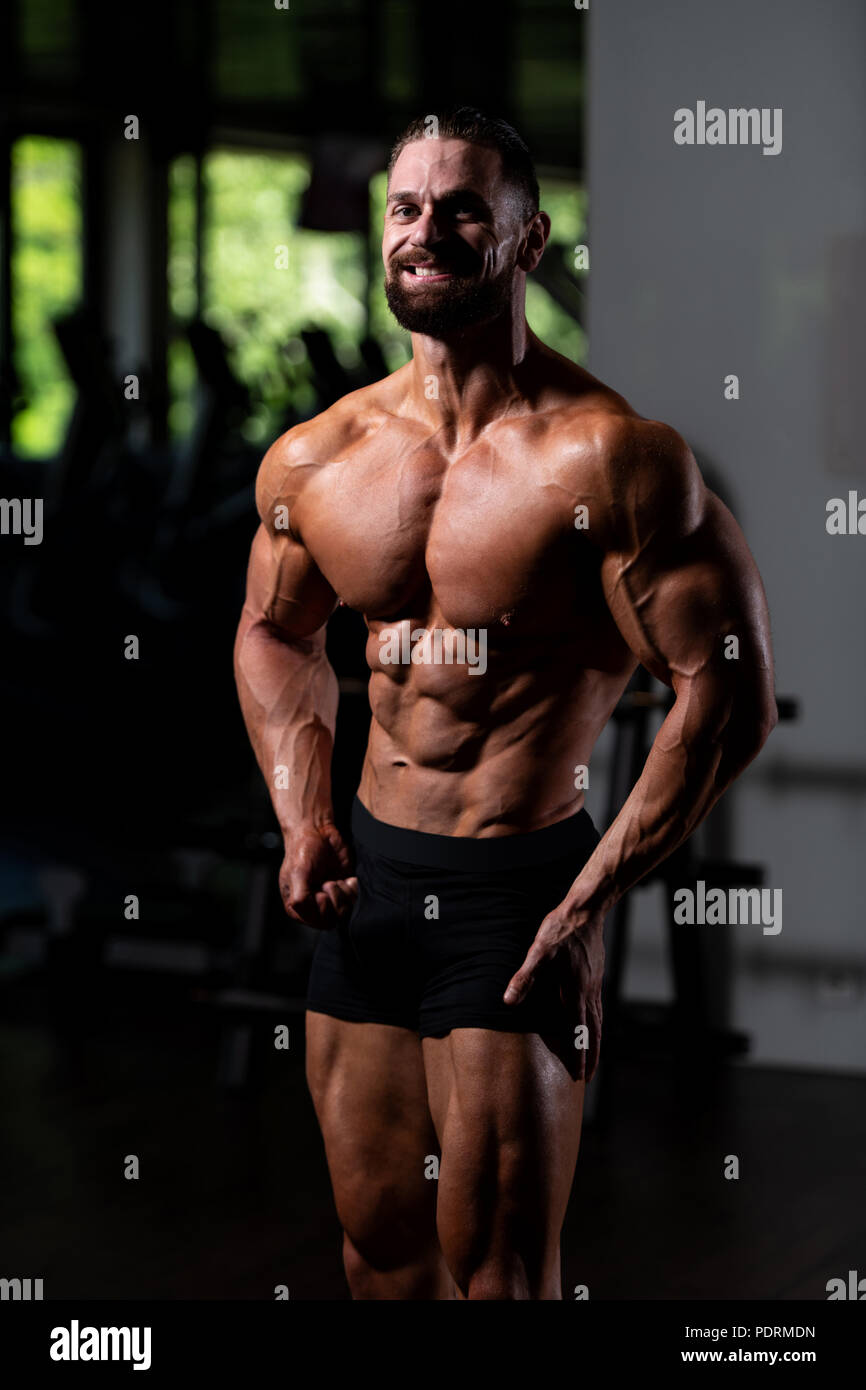 Young Man Standing Strong In The Gym And Flexing Muscles - Muscular Athletic  Bodybuilder Fitness Model Posing After Exercises Stock Photo - Alamy