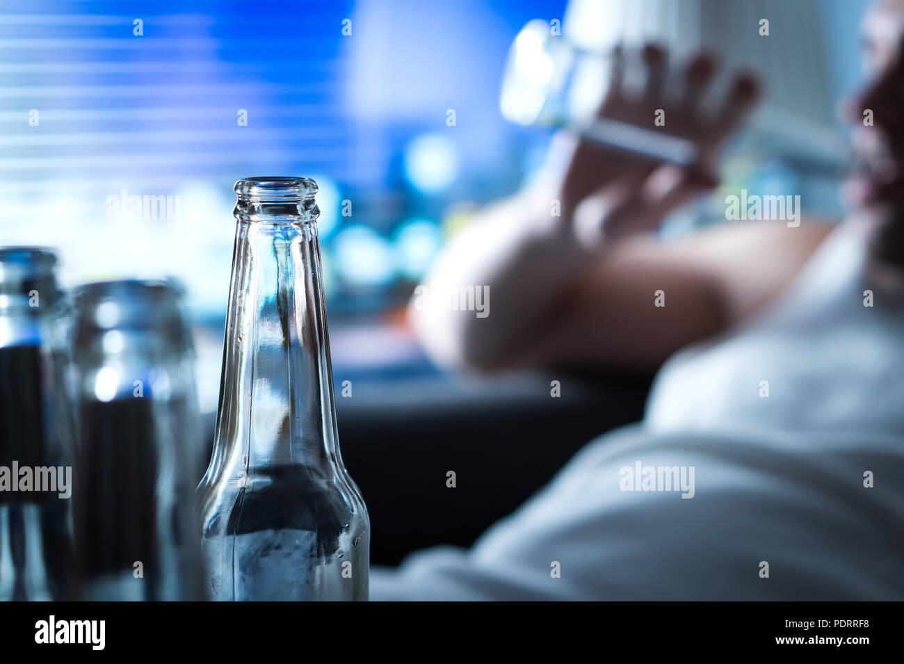 Anynomous alcoholic taking sip of beer. Home full of empty bottles. Alcoholism and drinking problem concept. Man sipping alcohol late at night. Stock Photo