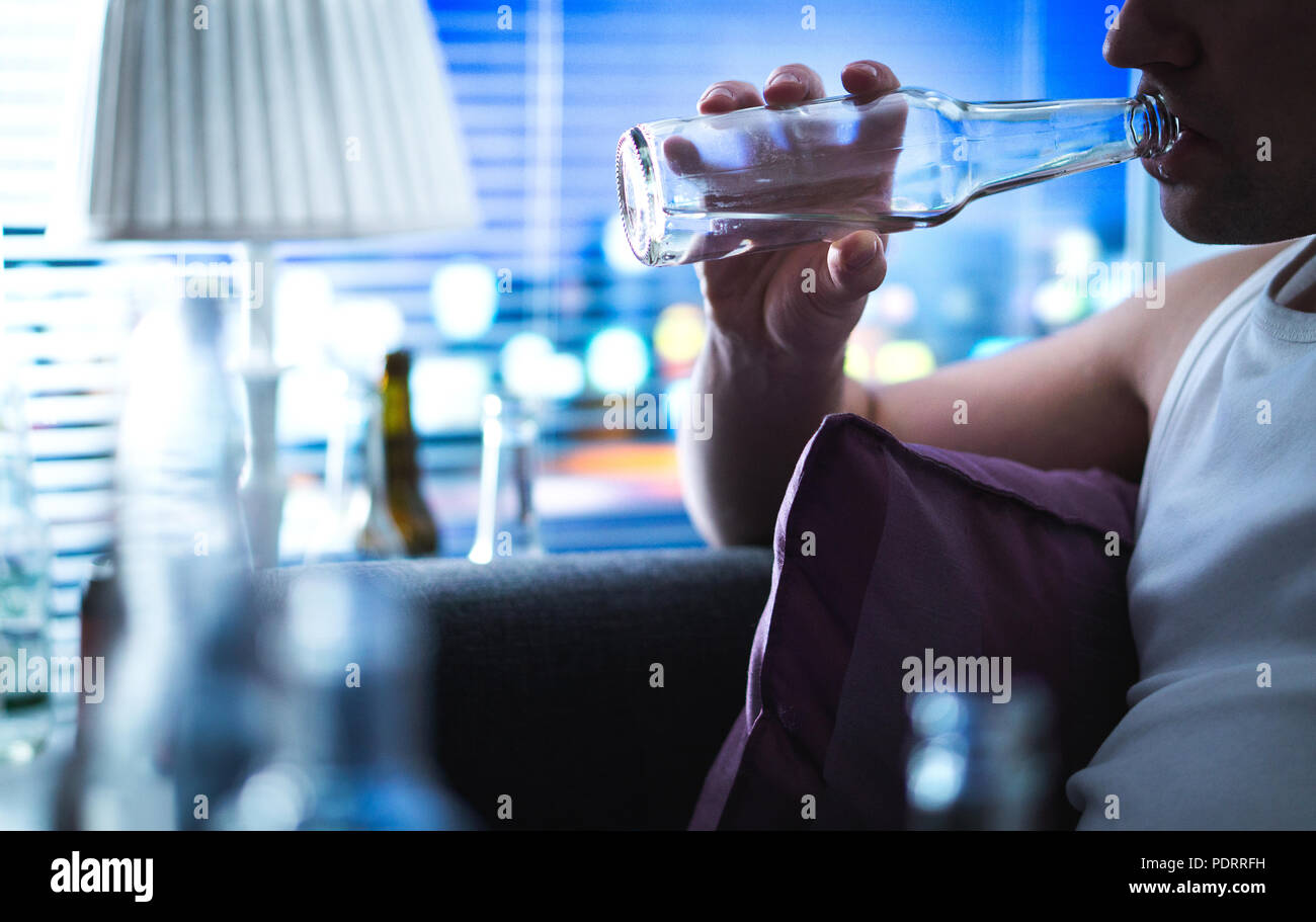 Alcoholic sipping bottle. Alcoholism and alcohol abuse concept. Drunken man sitting home on couch. Unemployed sad guy drinking on sofa. Stock Photo