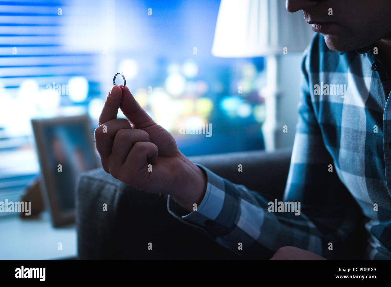 Divorce, relationship problems, being single or regret concept. Serious sad man looking at wedding or engagement ring home late at night. Stock Photo