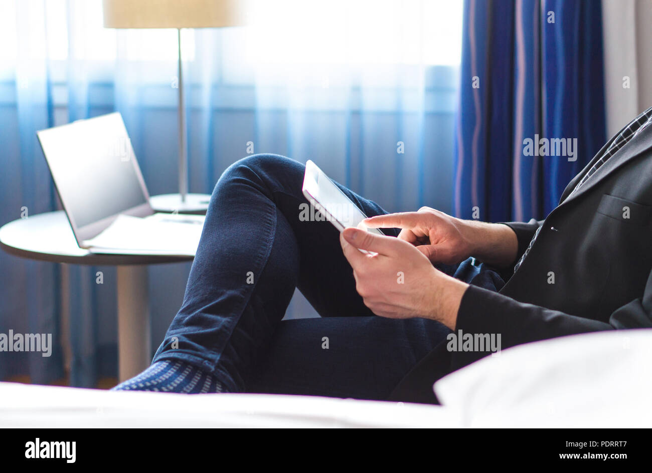 Business man reading news or email with tablet in hotel room. Businessman using smart mobile device and relaxing. Stock Photo