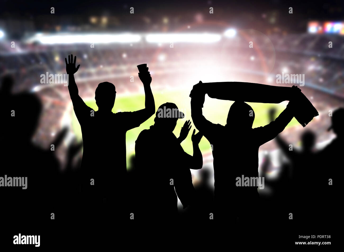 Friends at football game in soccer stadium. Crowd cheering and celebrating a goal in arena during match. Silhouette people in live sport audience. Stock Photo