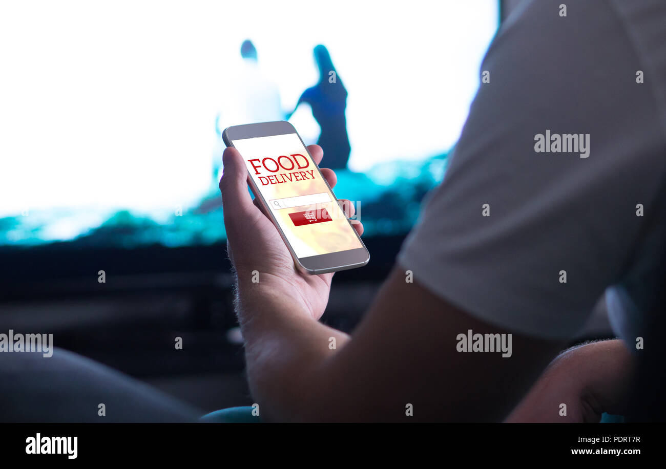 Take away food order online with delivery app and smartphone. Man buying pizza or fast food home while watching TV. Stock Photo