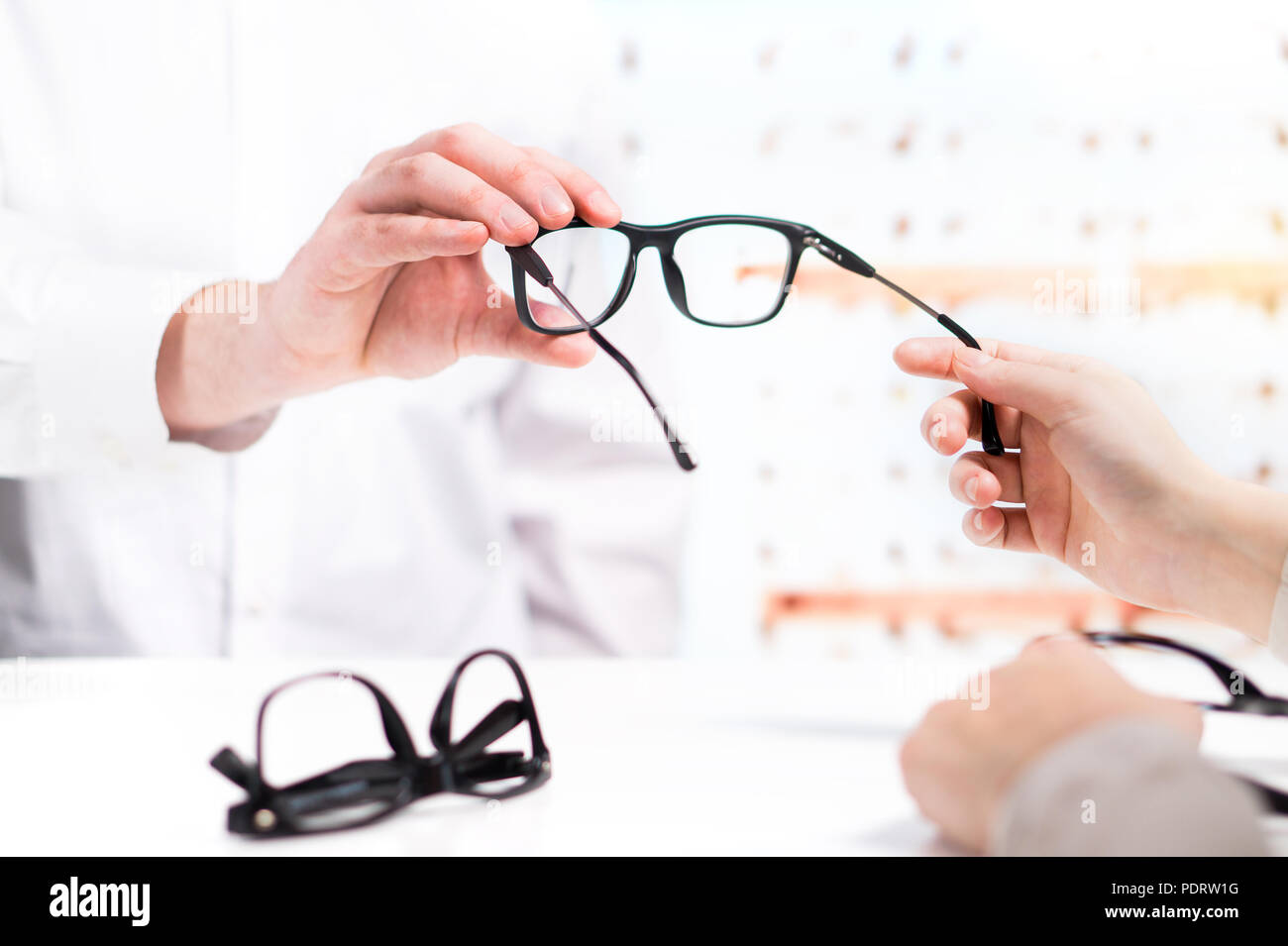 Optician giving new glasses to customer for testing and trying. Eye doctor with client comparing spectacles and choosing lenses in store. Stock Photo