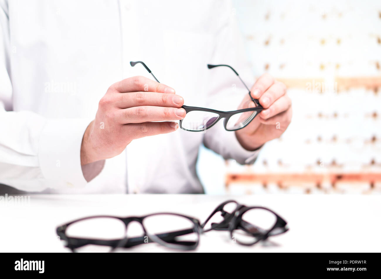 Optician in store holding glasses. Eye doctor with lenses. Professional optometrist in white coat with many eyeglasses. Shop interior. Stock Photo