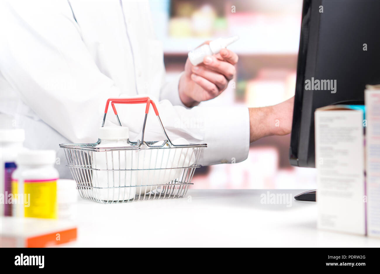 Pharmacy cashier or clerk at counter. Pharmacist using cash register. Druggist with pill bottles in shopping basket in drug store. Stock Photo