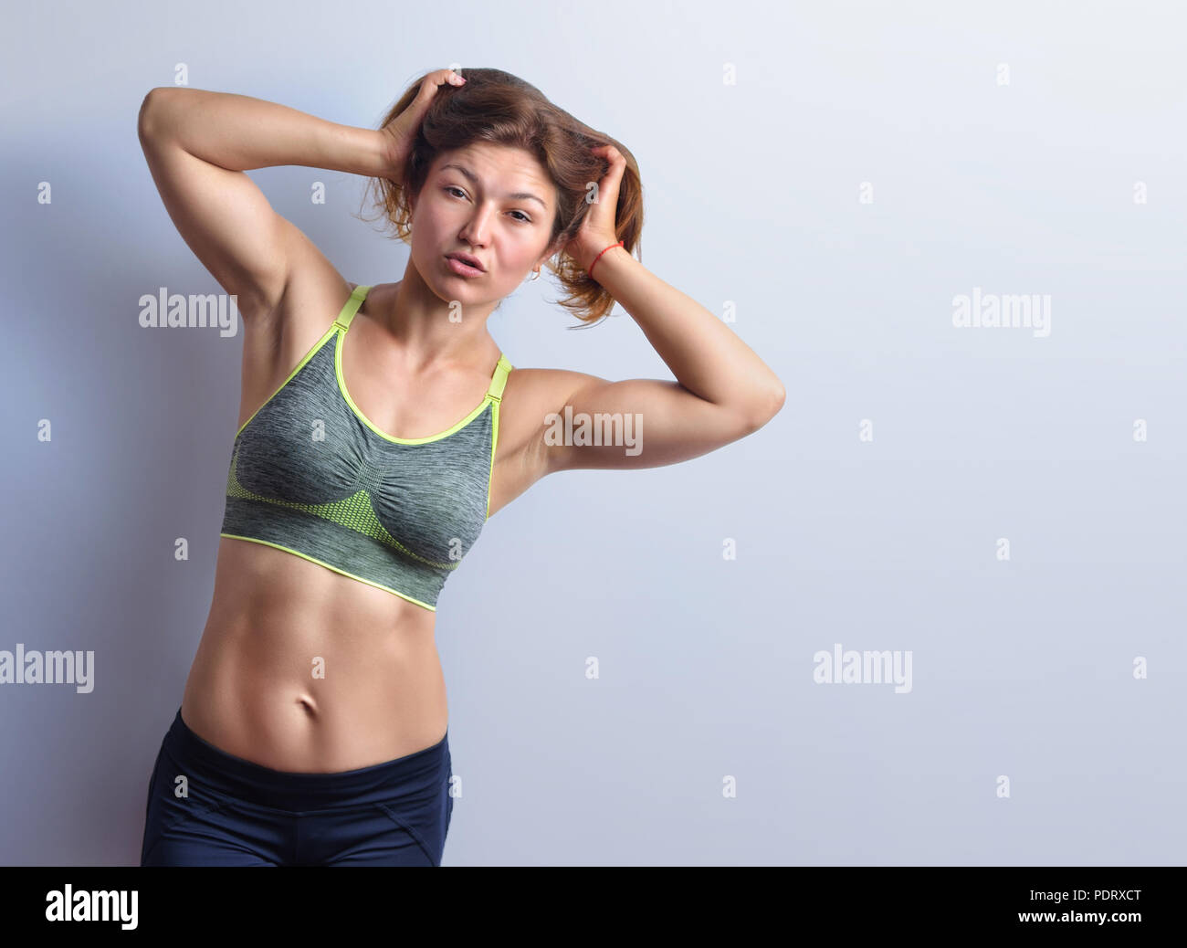 Slim female fitness coach in grey top and black leggings is posing on the  studio background,  front view. Stock Photo