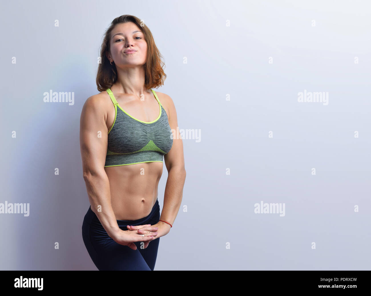 Slim young fitness woman showing muscles in a grey top black leggings isolated on a white background. Stock Photo