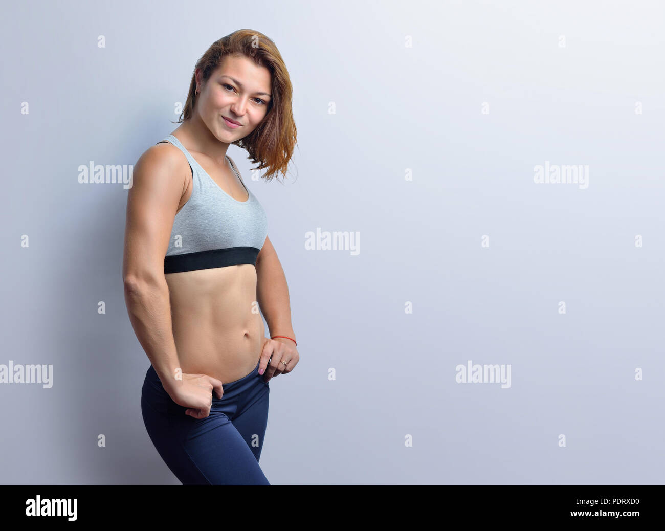 Female fitness coach showing muscles in a grey top and black leggings isolated on a white background. Stock Photo