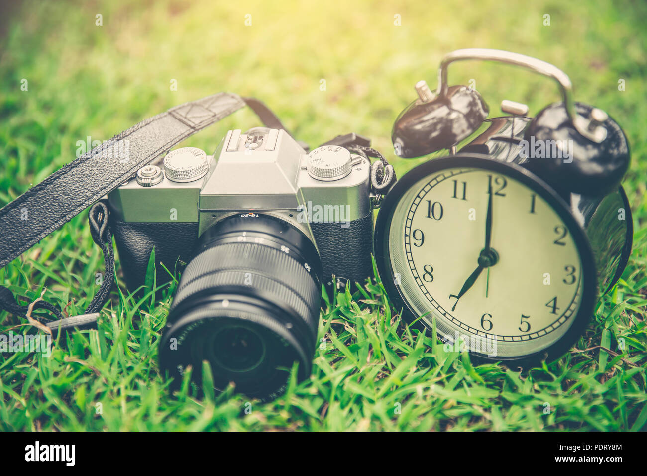 Photography times concept, mirrorless vintage camera with old bell clock on grass outdoor. Stock Photo