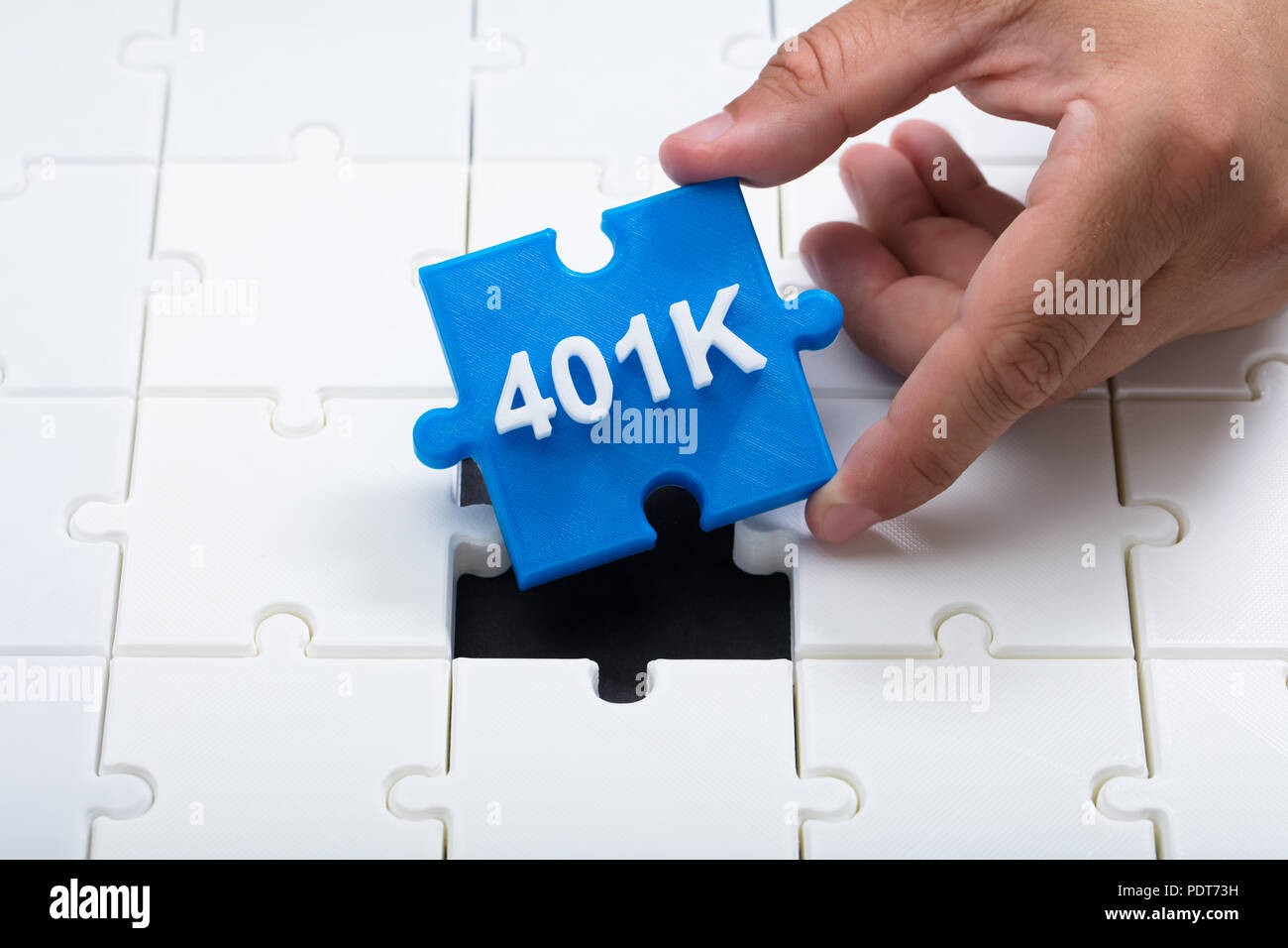 Close-up of a man's hand placing final blue 401k piece into jigsaw puzzle Stock Photo