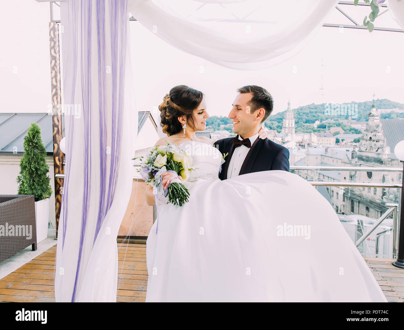 Horizontal phoro of the happy newlyweds. Groom carries the bride near the arch. Stock Photo