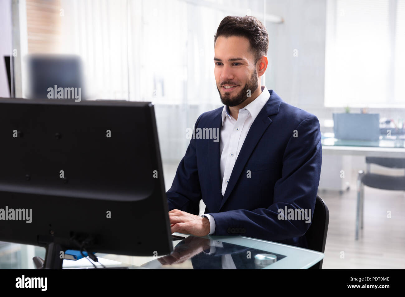 Smiling Young Businessman Using Computer In Office Stock Photo
