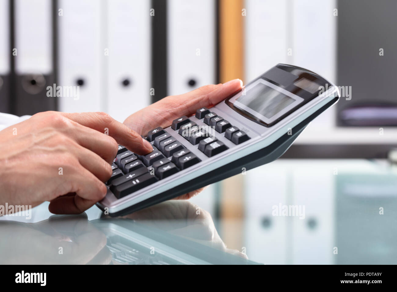 Businessperson's Hand Using Calculator Over Reflective Desk Stock Photo