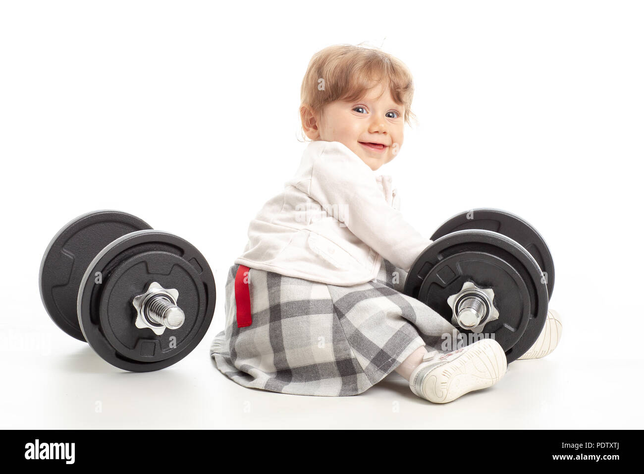 Small female baby playing with gym weights in studio shot on white background. Concept healty life in gym Stock Photo