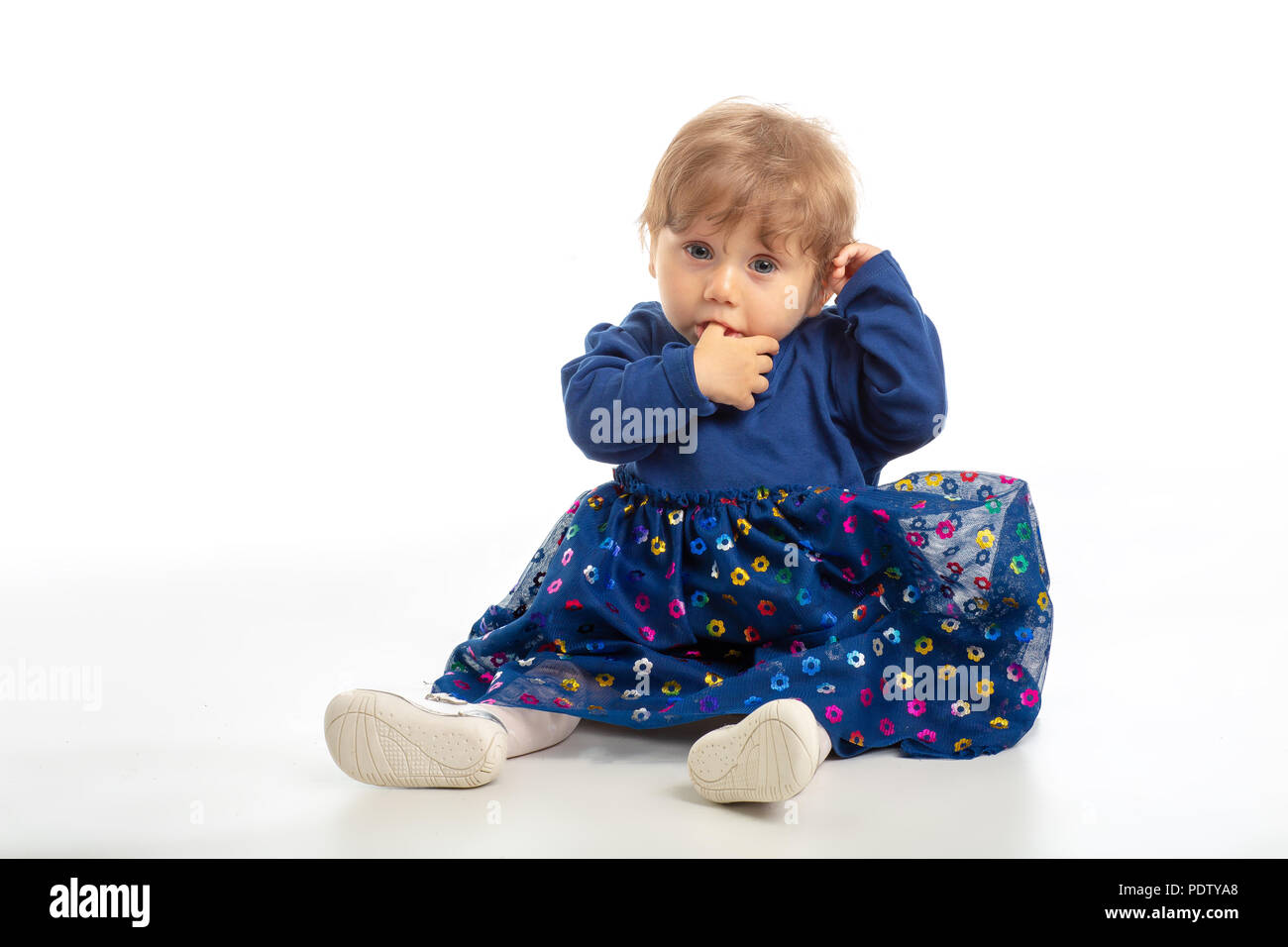 Elegant baby girl 1 year old sitting on the studio floor. White Background. Stock Photo