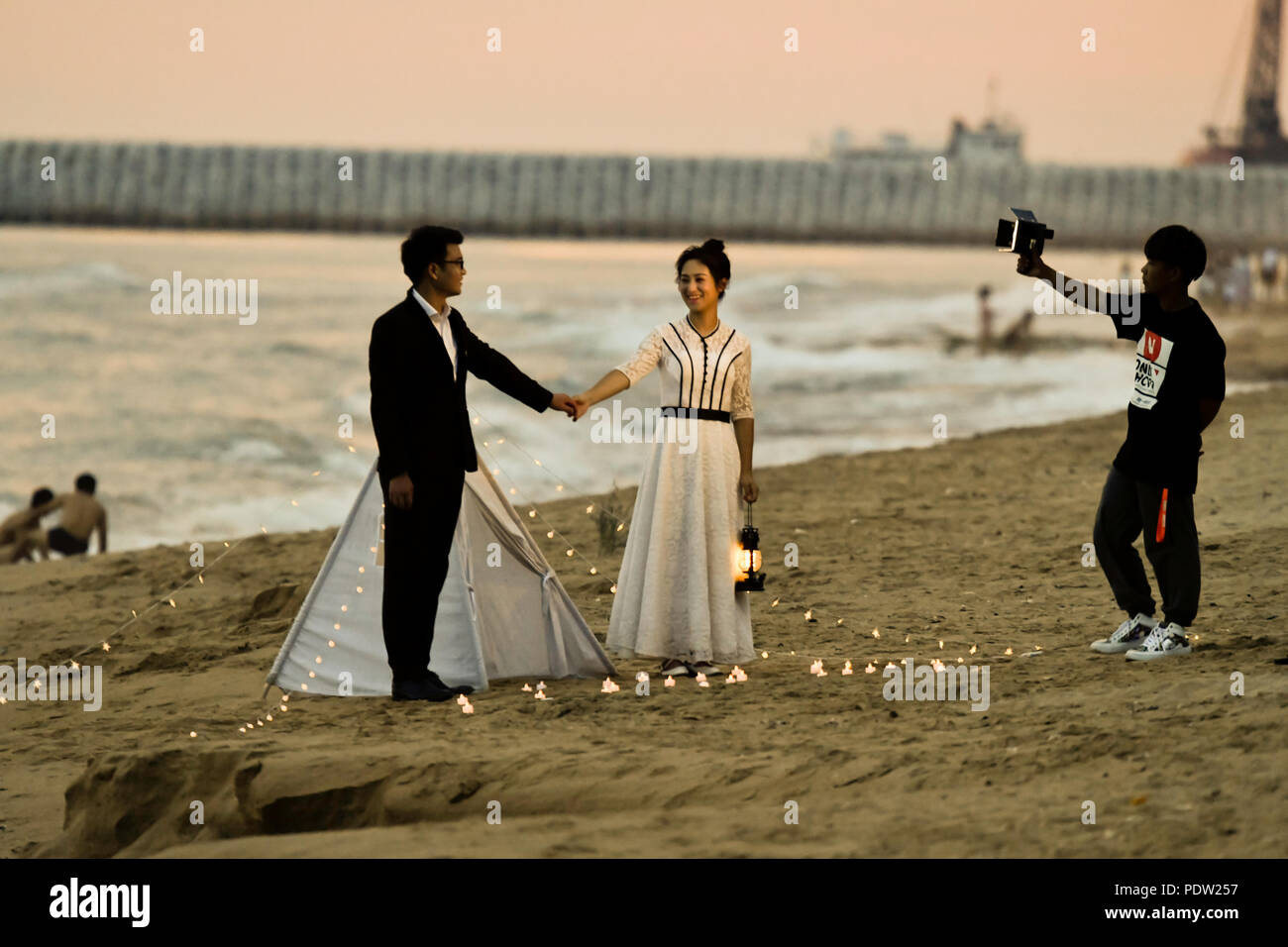 Wedding photography, on beach, sunset, camera, pose holding hands couple Stock Photo