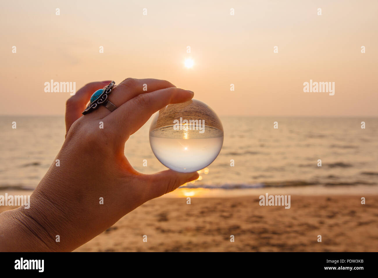 Crystal lens ball in hand with reflection of sea and sunset on the ...