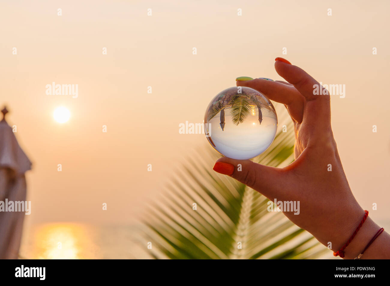 Crystal lens ball in hand with reflection of sea and sunset on the ...