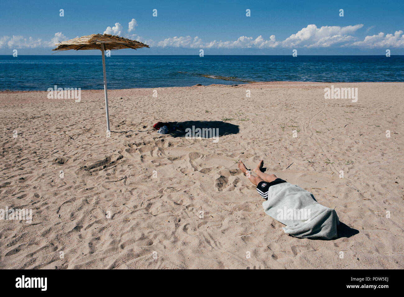 Man sleeping on a beach with a towel on his head, lake issyk kul in