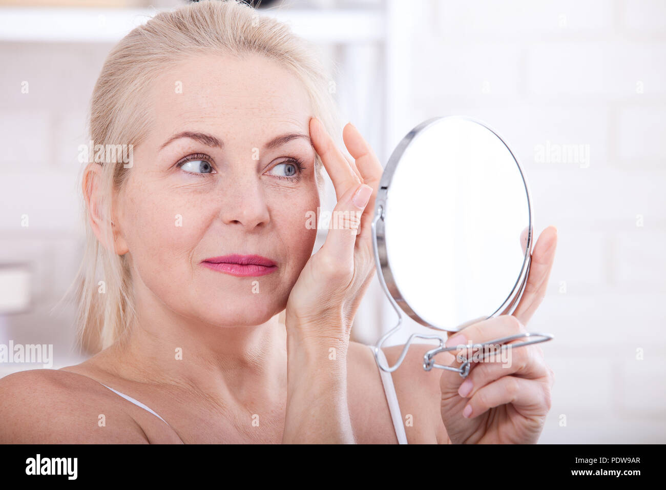 Forty years old woman looking at wrinkles in mirror. Plastic surgery and collagen injections. Makeup. Macro face. Selective focus on the face Stock Photo