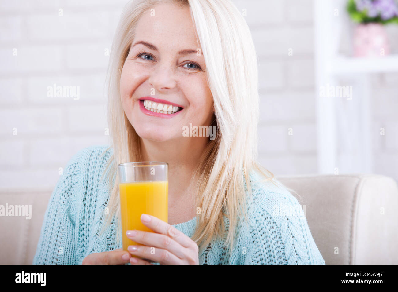 Woman drinking orange juice smiling. Beautiful middle aged Caucasian model at home. Stock Photo