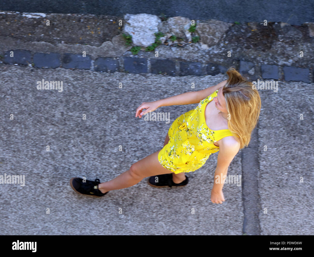 Looking down from high up to a cheerful and brightly dressed 16 year old blond haired girl walking through the old village streets of Cessenon Stock Photo