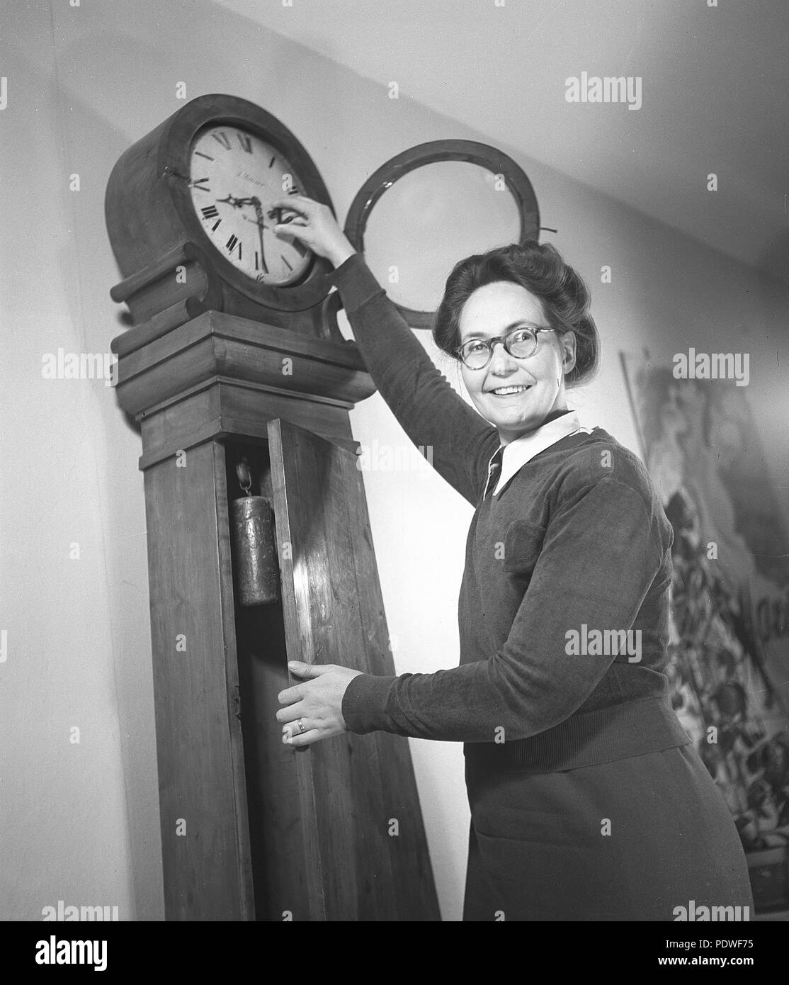1940s woman with glasses. An elderly lady is standing by a clock and changes to the right time. 1942. Photo Kristoffersson/N95-1 Stock Photo