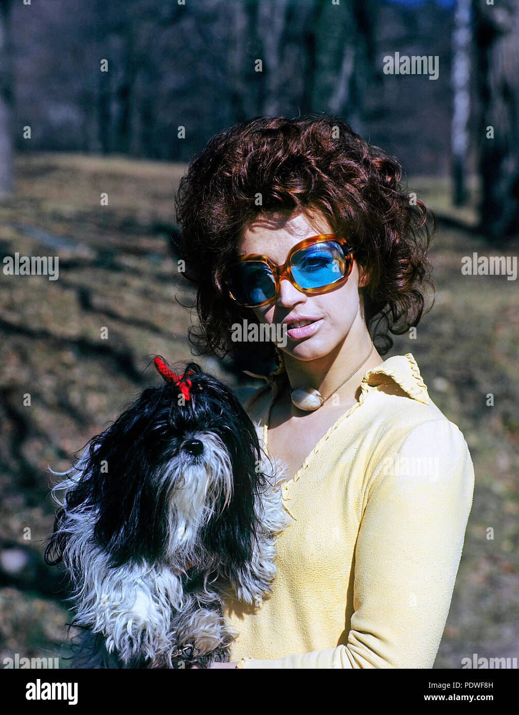 1970s glasses. A young woman in blue tainted sunglasses is holding her dog. 1971 Stock Photo