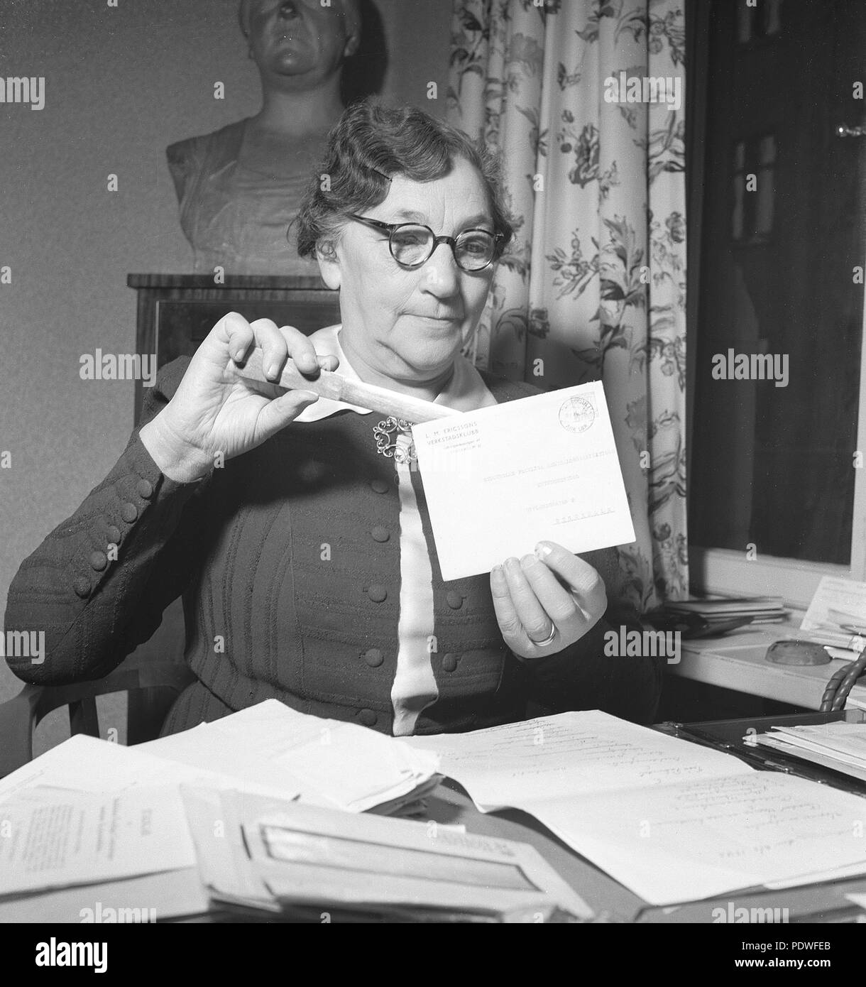 1940s woman with glasses. An older lady is opening an envelope with a letter knife. There are documents and letters on the office desk in front of her. 1942. Photo Kristoffersson/A83-4 Stock Photo