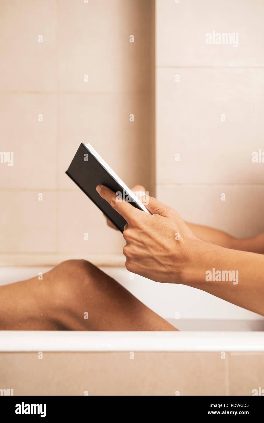 closeup of a young caucasian man reading a book while is taking a bath in the bathtub of a beige bathroom Stock Photo