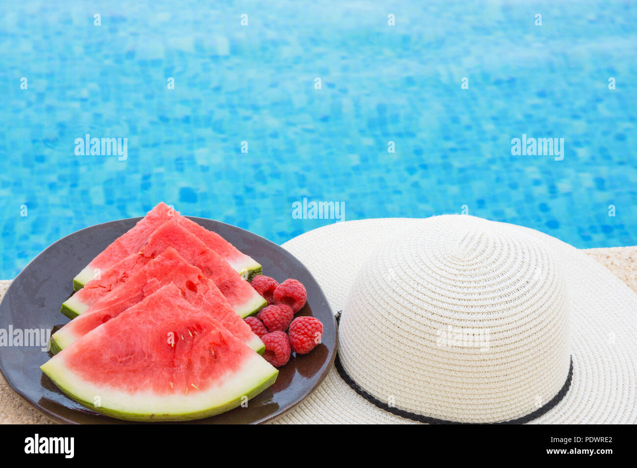 Wedges of Ripe Juicy Seedless Watermelon Raspberries on Plate on Rattan Table by Swimming Pool. Vacation Relaxation Summer Vibes. Authentic Atmosphere Stock Photo