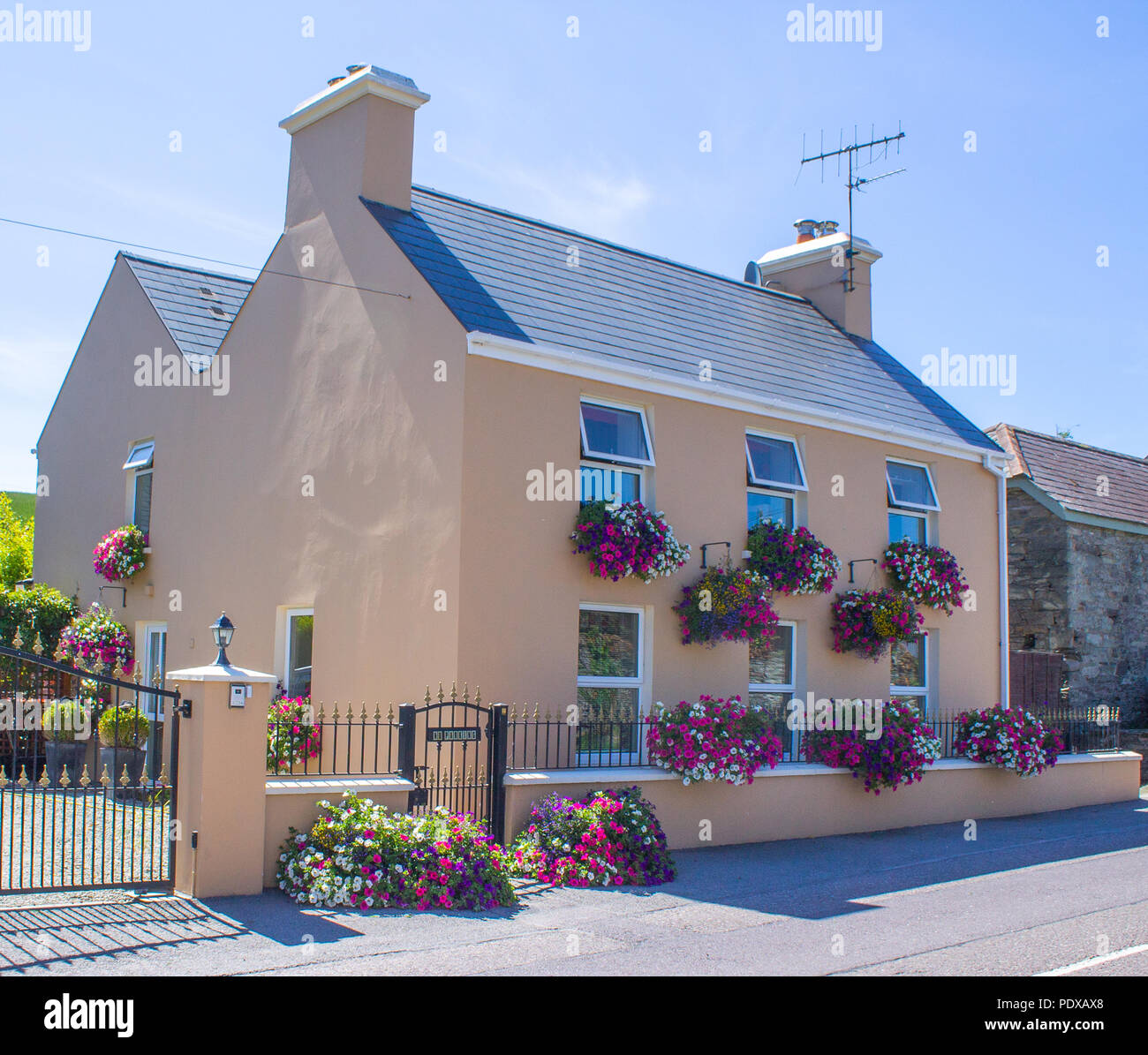 brightly painted house with baskets of summer flowers decorating it. West Cork , Ireland Stock Photo