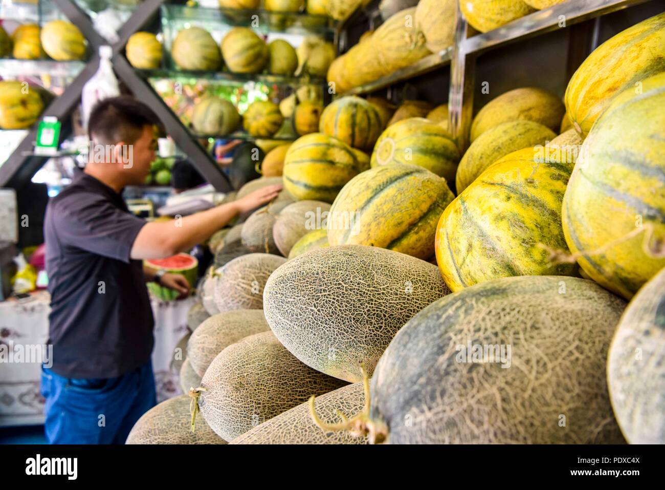 Urumqi, China's Xinjiang Uygur Autonomous Region. 9th Aug, 2018. A tourist selects cantaloupe at a bazaar in Urumqi, northwest China's Xinjiang Uygur Autonomous Region, Aug. 9, 2018. Xinjiang, enjoying the long sunshine duration and large temperature difference, is famous for its bounty of fruits, including grapes, melons, pears, etc. Credit: Zhao Ge/Xinhua/Alamy Live News Stock Photo