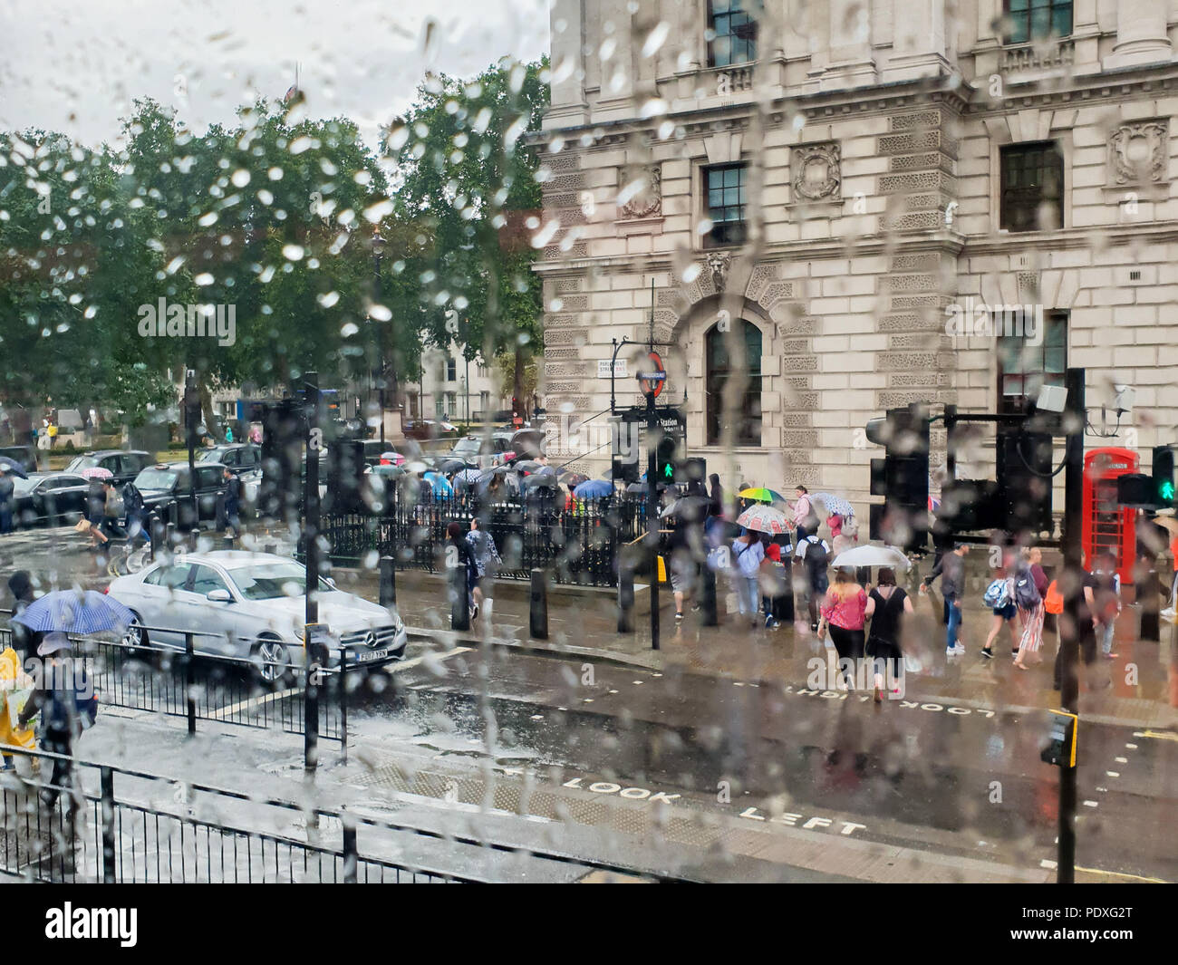 Westminster. London. UK 10 Aug 2018 - View of tourists with umbrellas on Whitehall through a double decker bus window covered with raindrops.  Credit Roamwithrakhee /17�Թ����� Live News Stock Photo