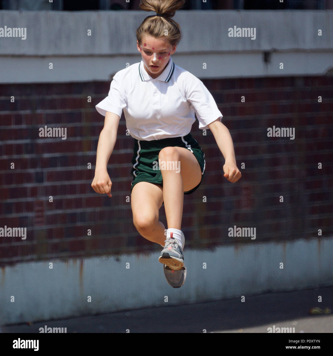Teenage girl in mid air doing the long jump for high school sports day