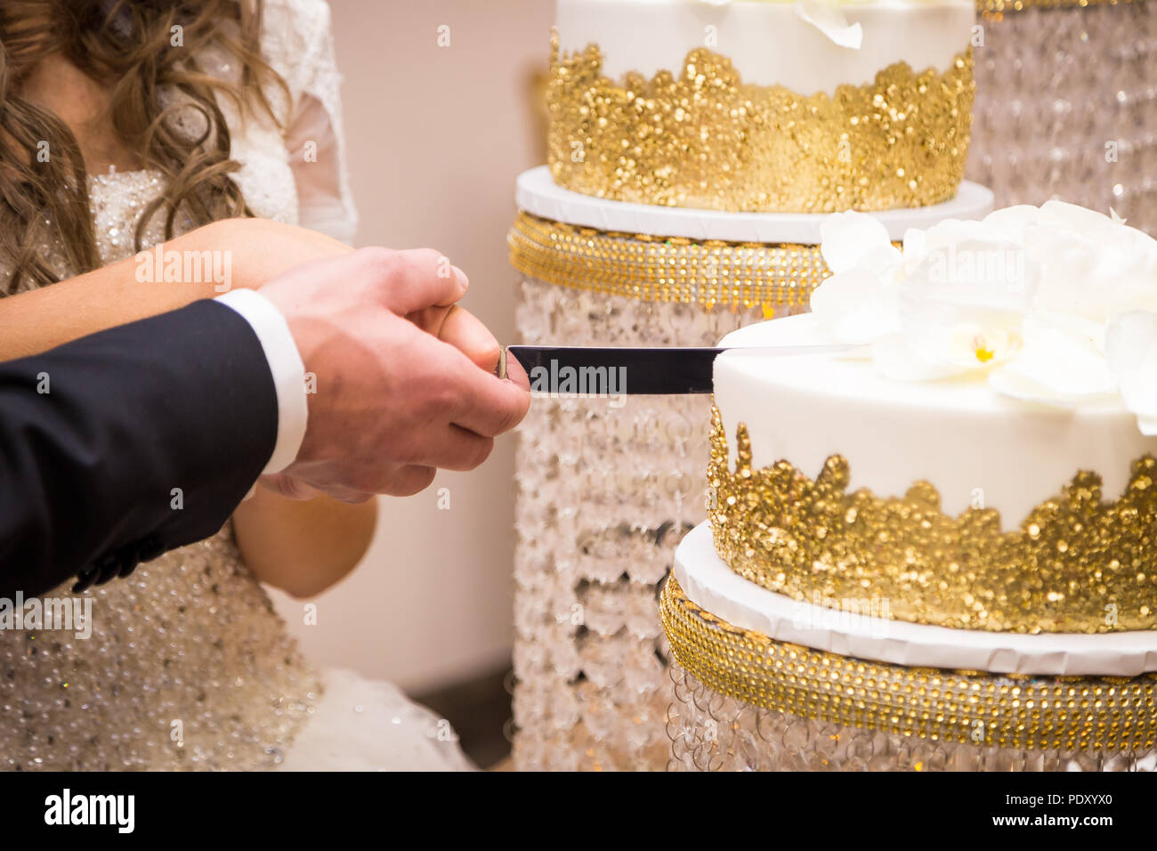 Close-up of a newlywed couple's hands cutting their wedding cake. Stock Photo