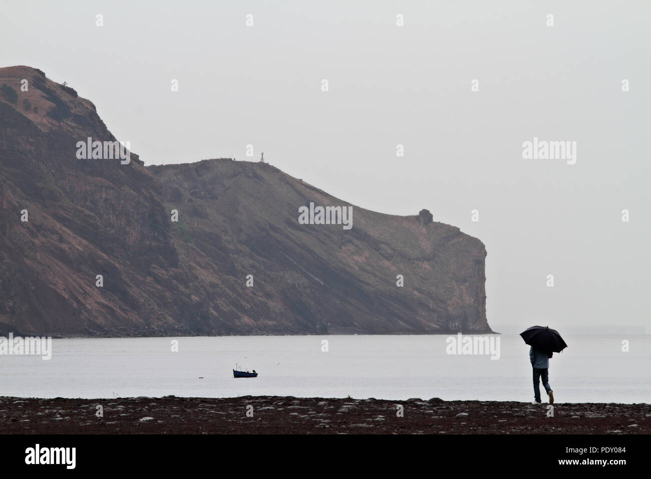 A man walking along the shore line on Madeira island on a rainy day Stock Photo