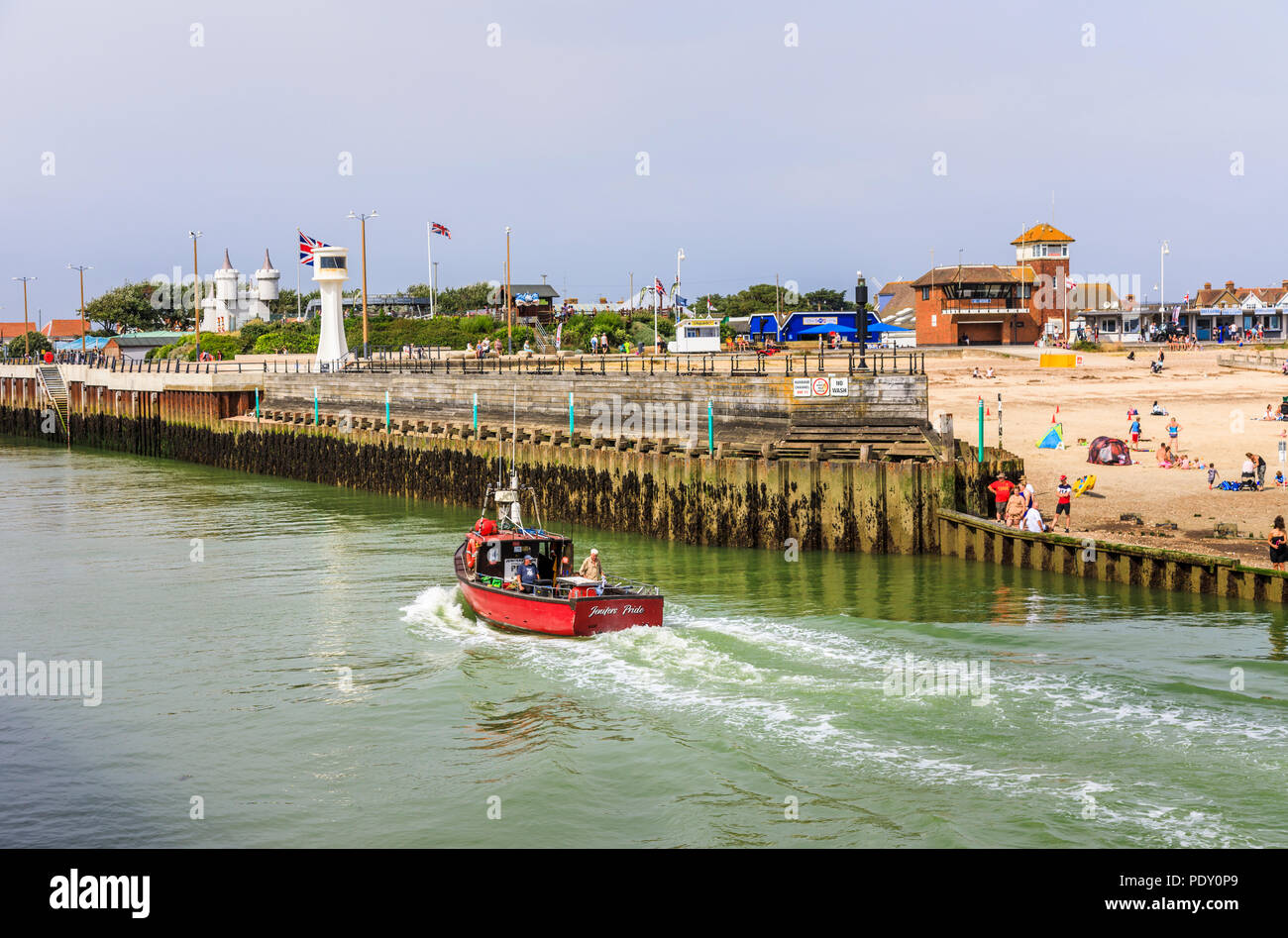 Small red fishing boat entering the River Arun by West Beach, Littlehampton, a small holiday resort on the south coast in West Sussex, UK in summer Stock Photo