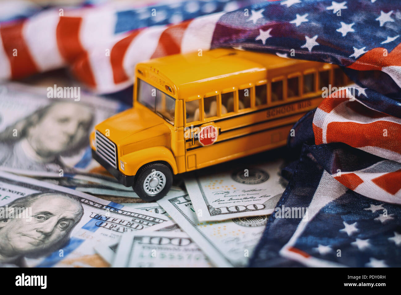 Yellow school bus children educational transport with signs in US dollar cash banknote money in American flag waving in the wind. Stock Photo