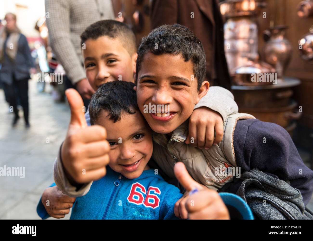 Three laughing children gleefully look at the camera and show a thumbs up, Shouk, Fez Medina, Fes, Morocco Stock Photo