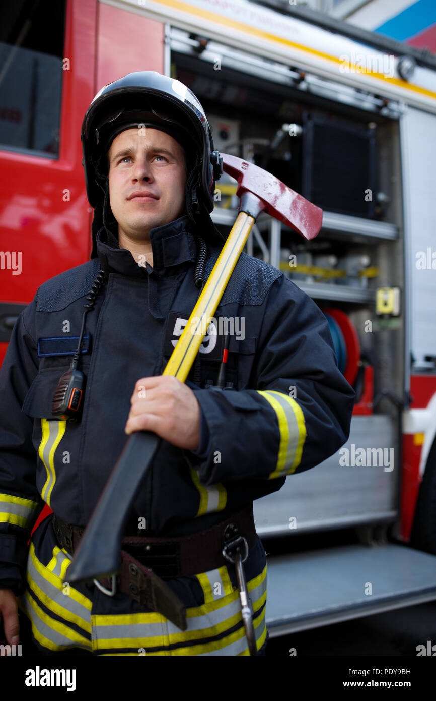Photo of serious fireman with hammer on background of fire engine at