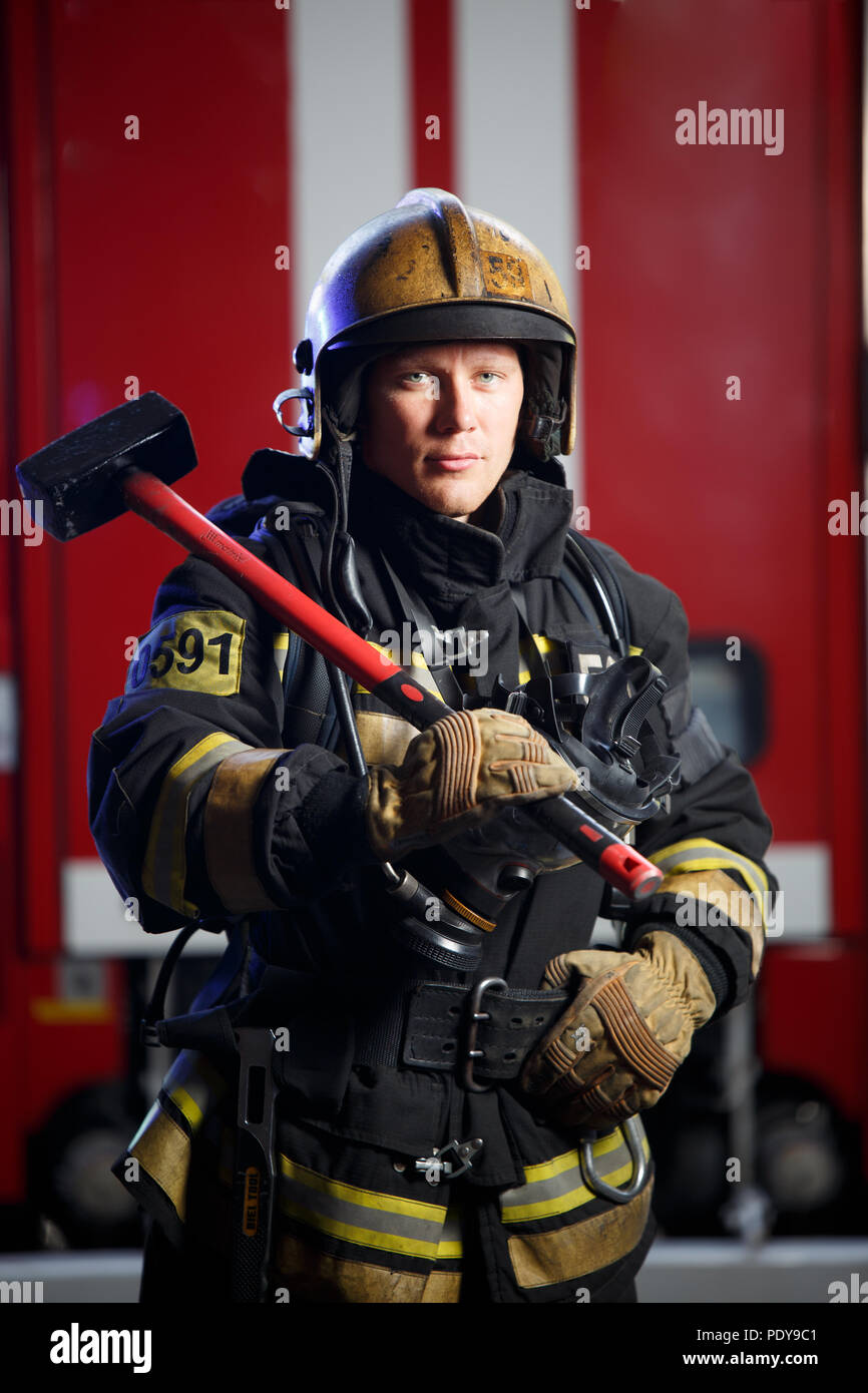 Photo of fireman with sledgehammer in hands near fire engine Stock